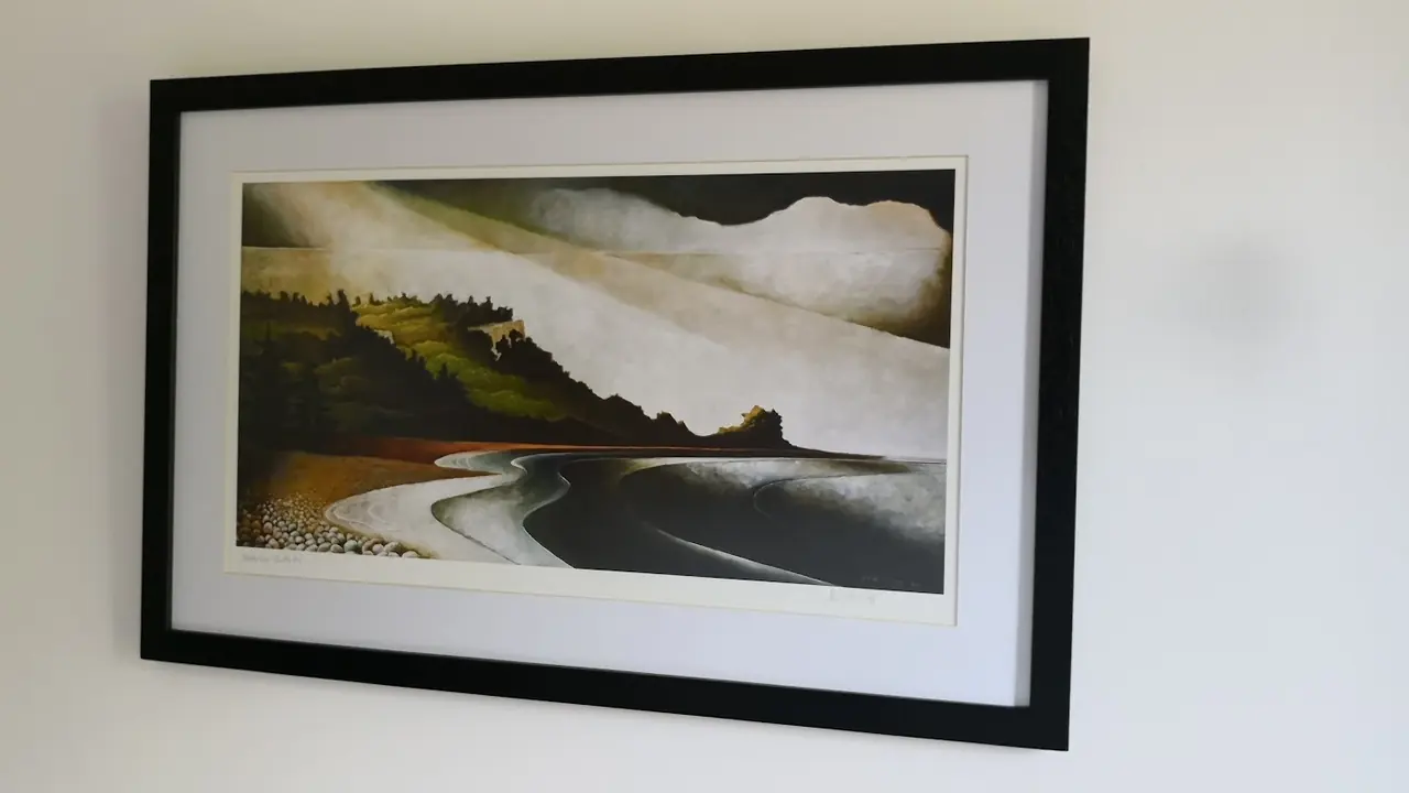 Coastal headland print in a wide black frame on a plain white wall